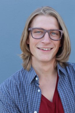 Mavi duvarın önünde uzun saçlı yakışıklı ve şık bir adamın yakın plan portresi.