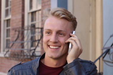 Bulanık şehir klasik arka planına sahip, telefon kullanan sarışın yakışıklı adamın yakın portresi.