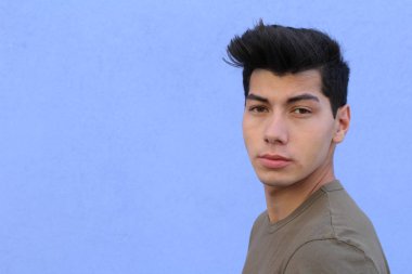 Mavi duvarın önünde poz veren yakışıklı genç adamın yakın plan portresi.