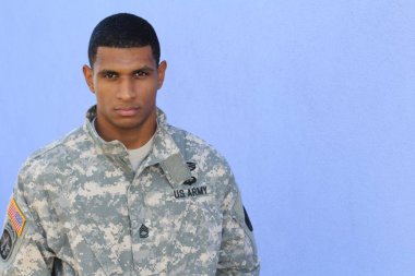 Mavi duvarın önünde üniformalı yakışıklı Afro-Amerikan askerinin yakın plan portresi