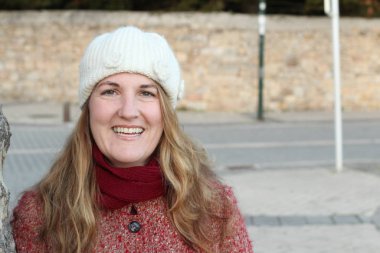 Kış giysileri içinde gülen sarışın kadının portresi gündüz vakti parkta duruyor.