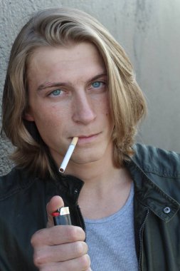 Sokakta sigara içen uzun saçlı yakışıklı bir adamın yakın plan portresi.