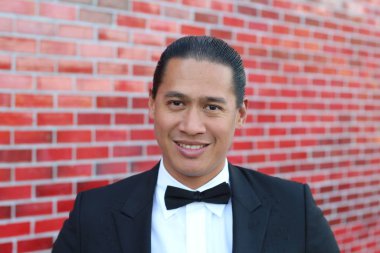 Kırmızı tuğla duvarın önünde papyonlu yakışıklı Asyalı bir adamın yakın plan portresi.