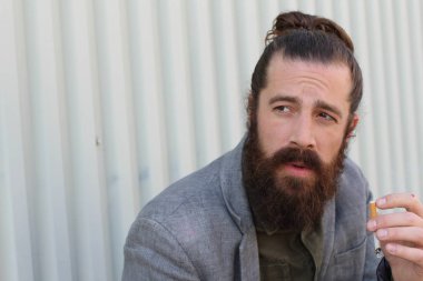 Sigara içen yakışıklı sakallı adamın portresi. Erkek saçı olan hippi..