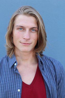 Mavi duvarın önünde uzun sarı saçlı yakışıklı genç adamın yakın plan portresi.