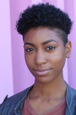 Mor duvar arkasında kısa kıvırcık saçlı güzel bir Afrikalı kadının yakın plan portresi. 