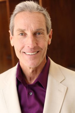 Bej ceketli yakışıklı olgun bir adamın kameraya bakarken yakın plan portresi.