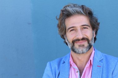 Mavi takım elbiseli ve mavi gömlekli yakışıklı bir iş adamının mavi duvarın önünde yakın plan portresi.