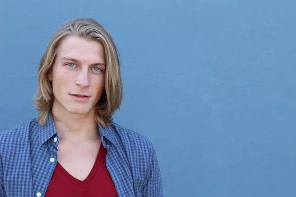 close-up portrait of handsome young man with long blonde hair in front of blue wall