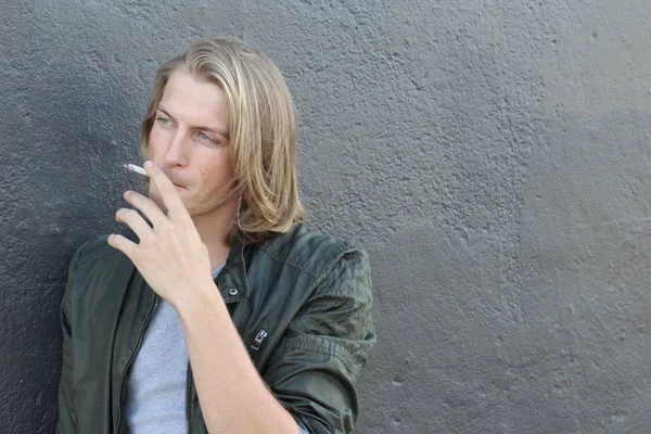 Sokakta sigara içen uzun saçlı yakışıklı bir adamın yakın plan portresi.