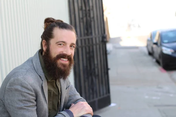 Stylish bearded hipster model with man bun hairstyle, lifestyle in the street, depth of field