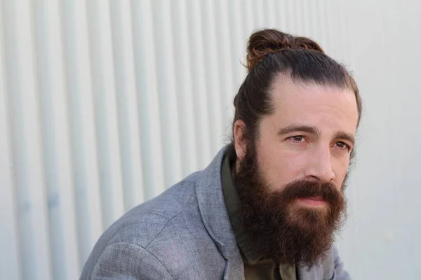 Stylish bearded hipster model with man bun hairstyle, lifestyle in the street, depth of field