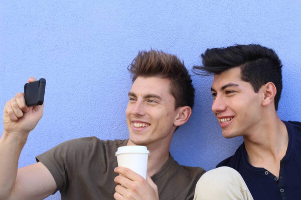 portrait of handsome young men taking selfie with smartphone in front of blue wall