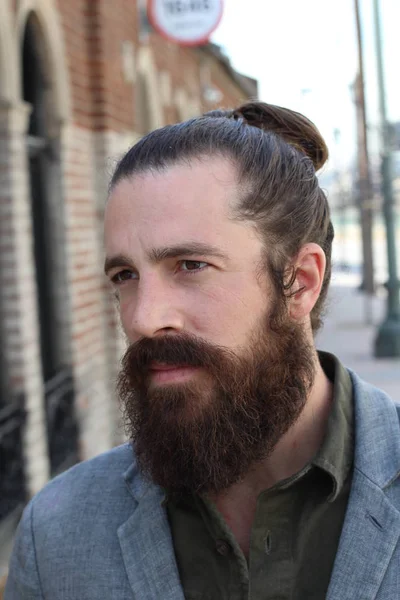 Stylish bearded hipster model with man bun hairstyle, lifestyle in the street, depth of field