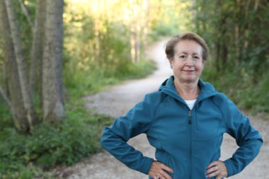 Ellerini beline dolamış, ormanda yürüyüş yapan mutlu bir son sınıf kadını.