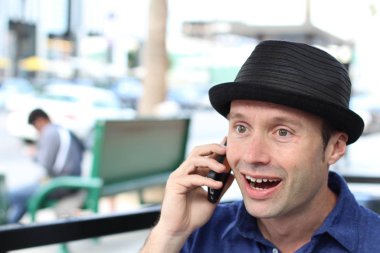 Şapkalı şık adam dışarıda telefonla konuşuyor.