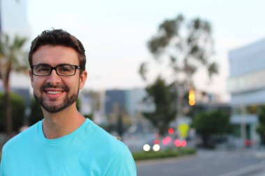 Açık havada duran, arka planda bulanık gözlüklü yakışıklı bir adam portresi.