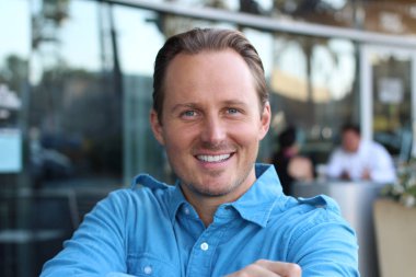 Kafede oturan ve kameraya bakan adam.