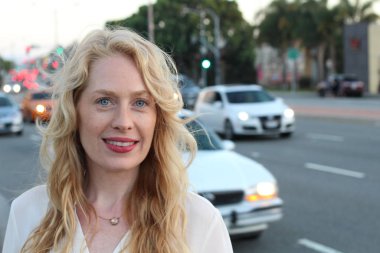 Akşam vakti şehirde caddede dikilen olgun sarışın kadın. 