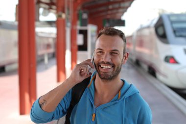 Tren istasyonunda trenini beklerken telefonda konuşan yakışıklı sakallı adam.