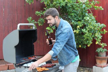Genç sakallı adamın açık havada gündüz vakti bahçede BBQ 'da yemek pişirme portresi. 
