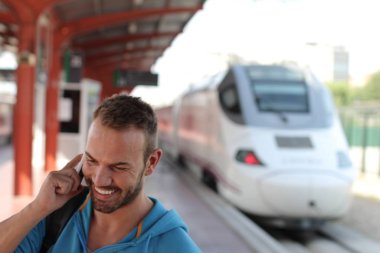 Tren istasyonunda trenini beklerken telefonda konuşan yakışıklı sakallı adam.