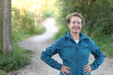Ellerini beline dolamış, ormanda yürüyüş yapan mutlu bir son sınıf kadını.