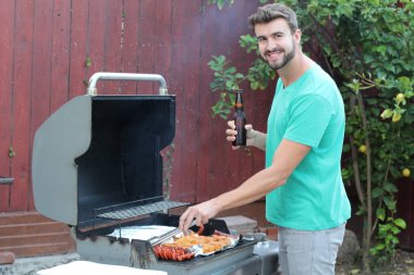 Genç sakallı adamın açık havada gündüz vakti bahçede BBQ 'da yemek pişirme portresi. 