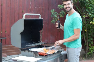 Genç sakallı adamın açık havada gündüz vakti bahçede BBQ 'da yemek pişirme portresi. 