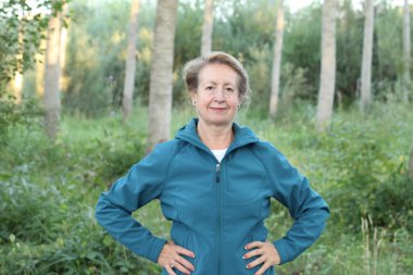 Ellerini beline dolamış, ormanda yürüyüş yapan mutlu bir son sınıf kadını.