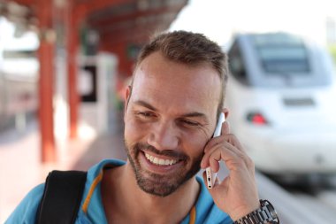 Tren istasyonunda trenini beklerken telefonda konuşan yakışıklı sakallı adam.
