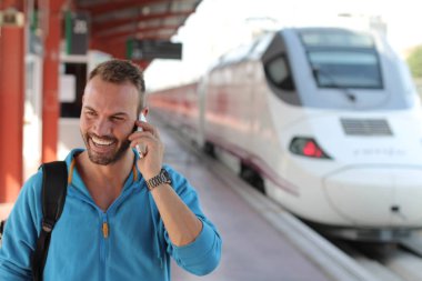 Tren istasyonunda trenini beklerken telefonda konuşan yakışıklı sakallı adam.