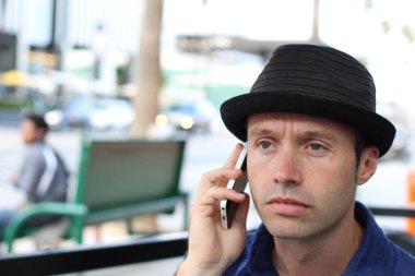 Şapkalı şık adam dışarıda telefonla konuşuyor.