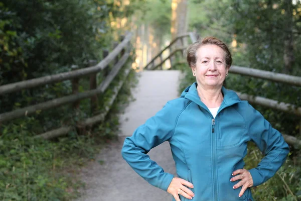 Happy senior woman with hands around waist hiking in woods