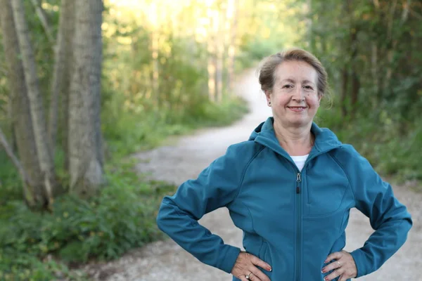 Happy senior woman with hands around waist hiking in woods