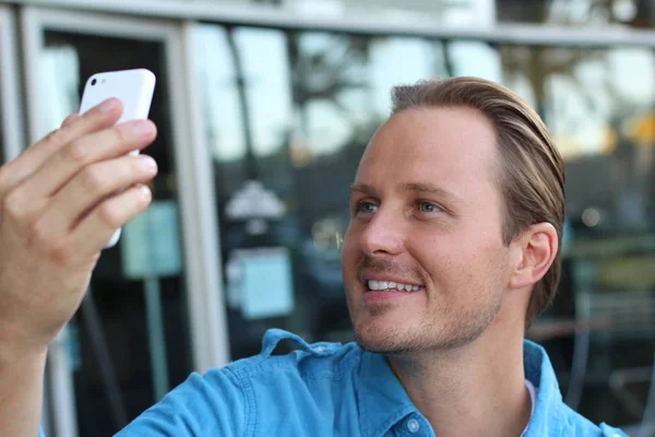 Young urban businessman using smartphone in bar, wearing a casual blue shirt