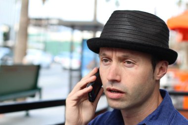 Şapkalı şık adam dışarıda telefonla konuşuyor.