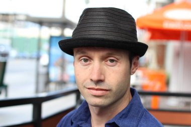 Şık şapkalı bir gencin açık hava portresi şehirde yürüyor, arka planı bulanık. 