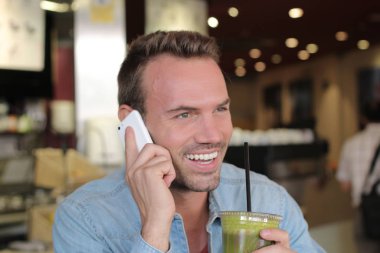 Restoranda smoothie içerken telefonla konuşan yakışıklı genç adamın yakın plan portresi.