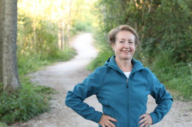 Ellerini beline dolamış, ormanda yürüyüş yapan mutlu bir son sınıf kadını.