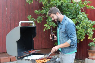 Genç sakallı adamın açık havada gündüz vakti bahçede BBQ 'da yemek pişirme portresi. 