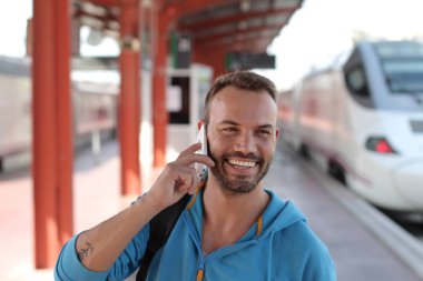 Tren istasyonunda trenini beklerken telefonda konuşan yakışıklı sakallı adam.