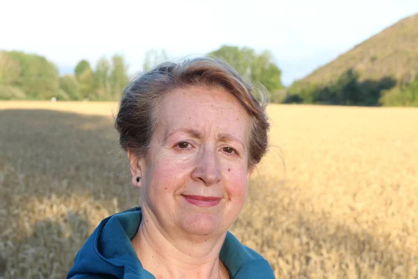 Free woman enjoying nature sunset. Freedom and serenity concept with mature natural female model. Caucasian female model in her 60s enjoying sunset from a wheat field