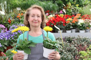 Güzel olgun bir kadının güzel renkli çiçeklerle dolu kaplarla yakın plan portresi.