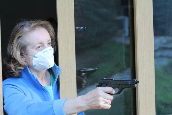 銃で窓から外を見る医療用保護マスクの美しい熟女のクローズアップ肖像 — ストック写真