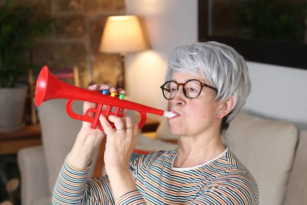 close-up portrait of mature woman with toy red trumpet sitting at home during quarantine