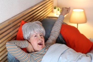 Olgun gri saçlı kadın evde yalnızlık çekerken yatakta geriniyor.