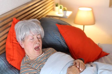 Olgun gri saçlı kadın evde yalnızlık çekerken yatakta dinleniyor.