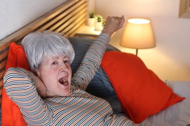 Olgun gri saçlı kadın evde yalnızlık çekerken yatakta geriniyor.