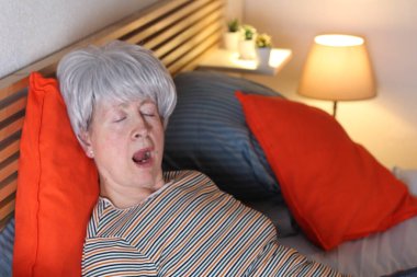 Olgun gri saçlı kadın evde yalnızlık çekerken yatakta esniyor.